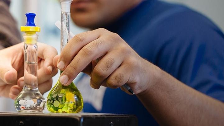 two hands hold two flasks with different colored liquids